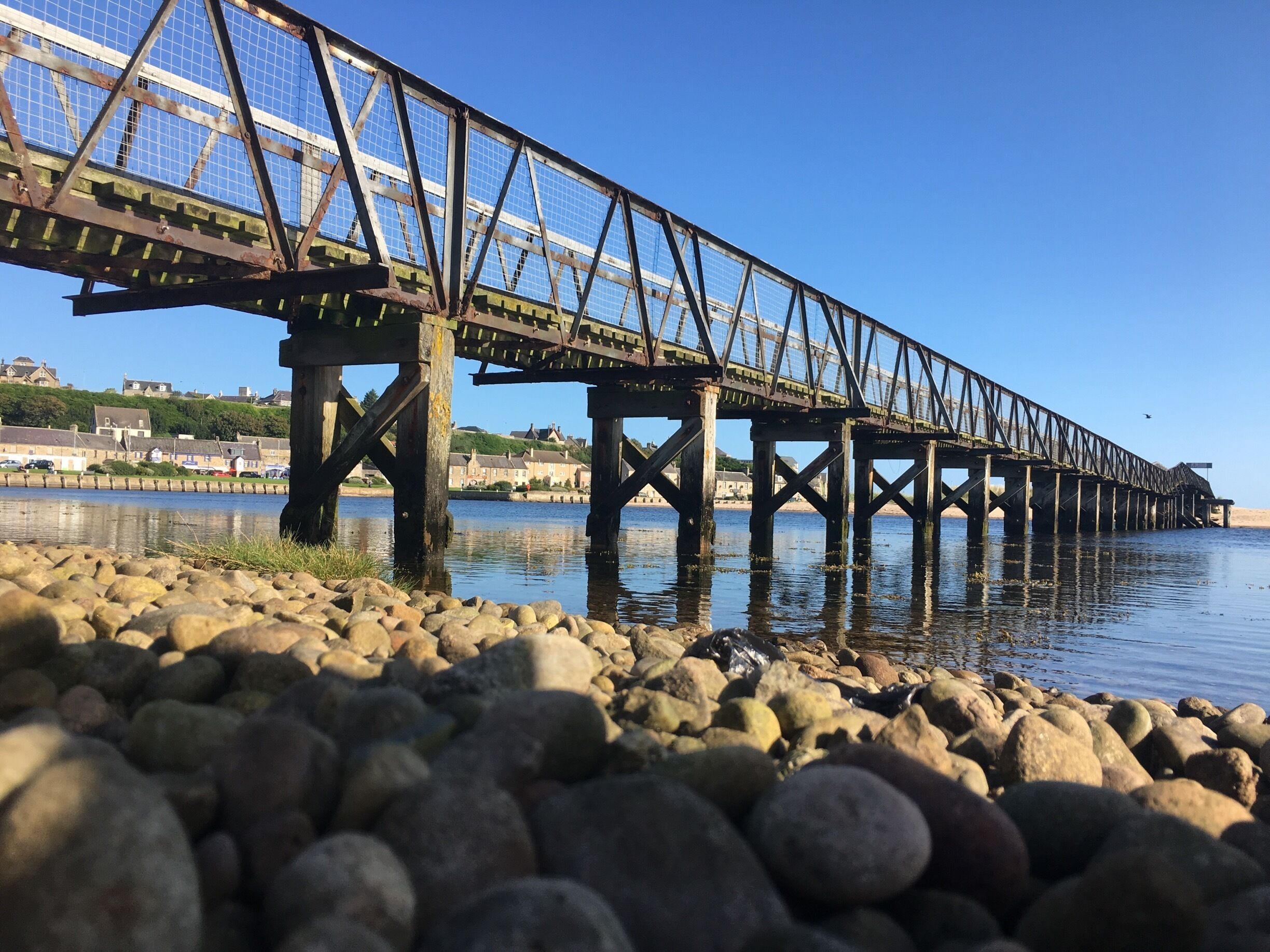 A steel bridge over a calm river with a rocky shoreline.