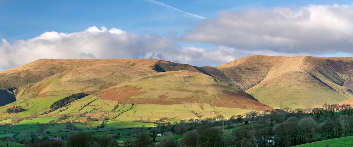 Rolling hills with a mix of green and brown terrain, a clear sky with clouds, and a few scattered trees.