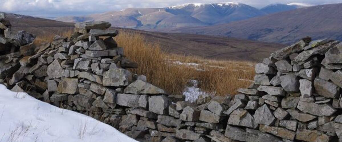 A stone wall, a snowy landscape, and distant mountains.