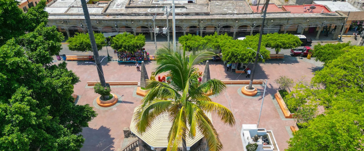 An aerial view of a plaza with palm trees, a central monument, and surrounding buildings.
