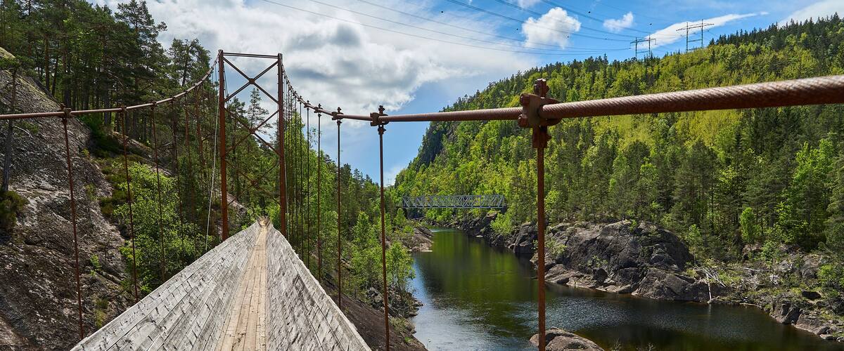 A wooden bridge over a river with a forested hillside in the background.