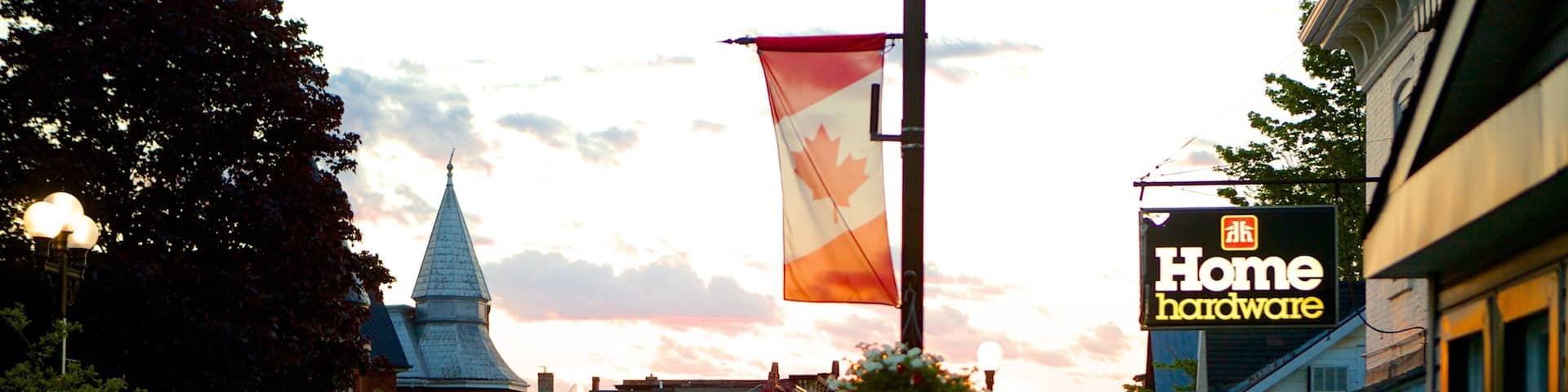 A street with a Canadian flag, a Home Hardware store, and a church with a steeple.