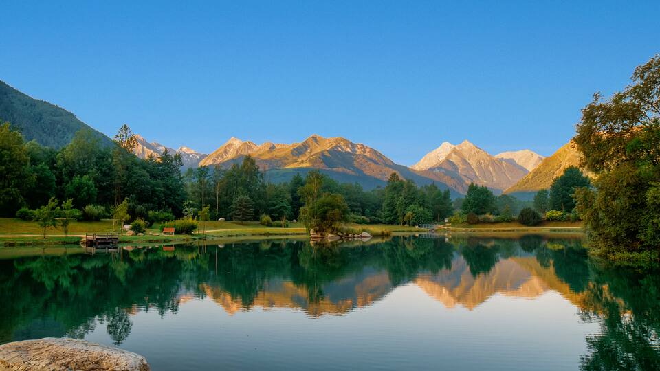 A tranquil lake with clear reflections of surrounding mountains and trees.