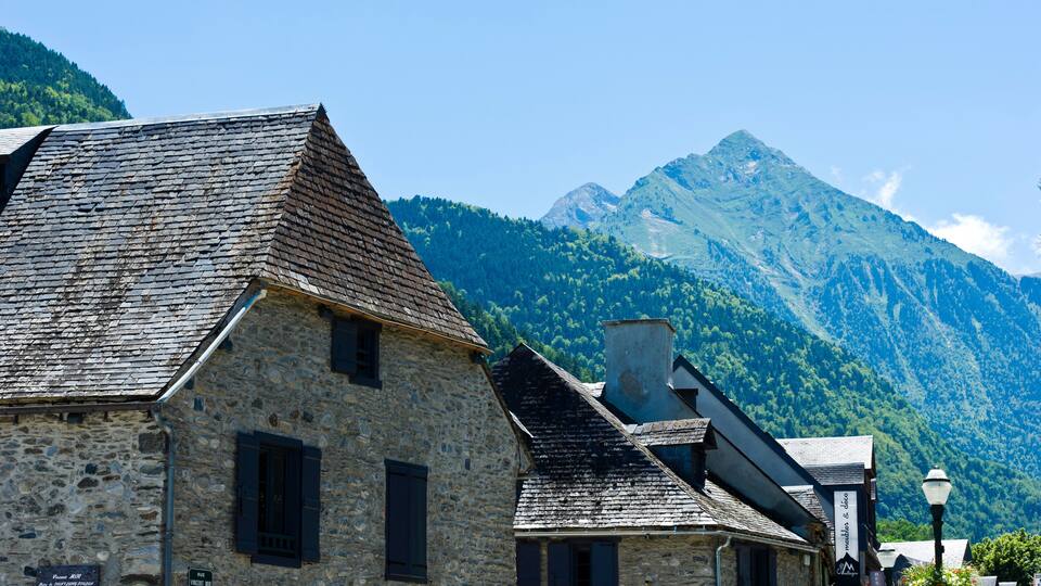 A stone building with a steep roof, a mountain in the background, and a clear blue sky.