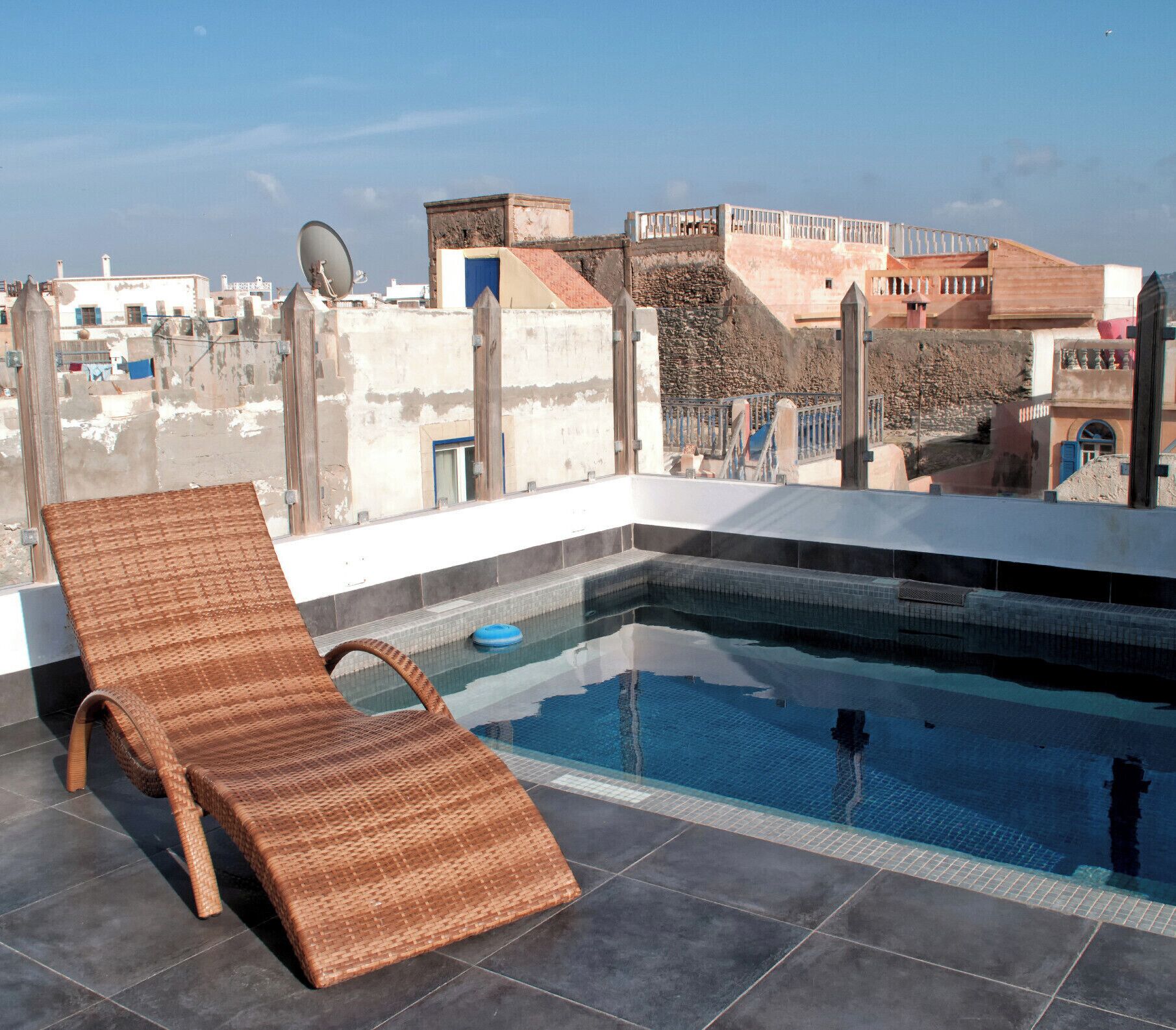 Una piscina en la azotea con una silla de mimbre, rodeada por un paisaje urbano con edificios históricos.