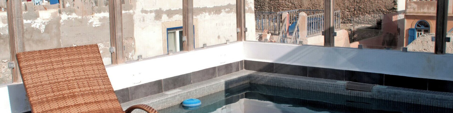 Una piscina en la azotea con una silla de mimbre, rodeada por un paisaje urbano con edificios históricos.