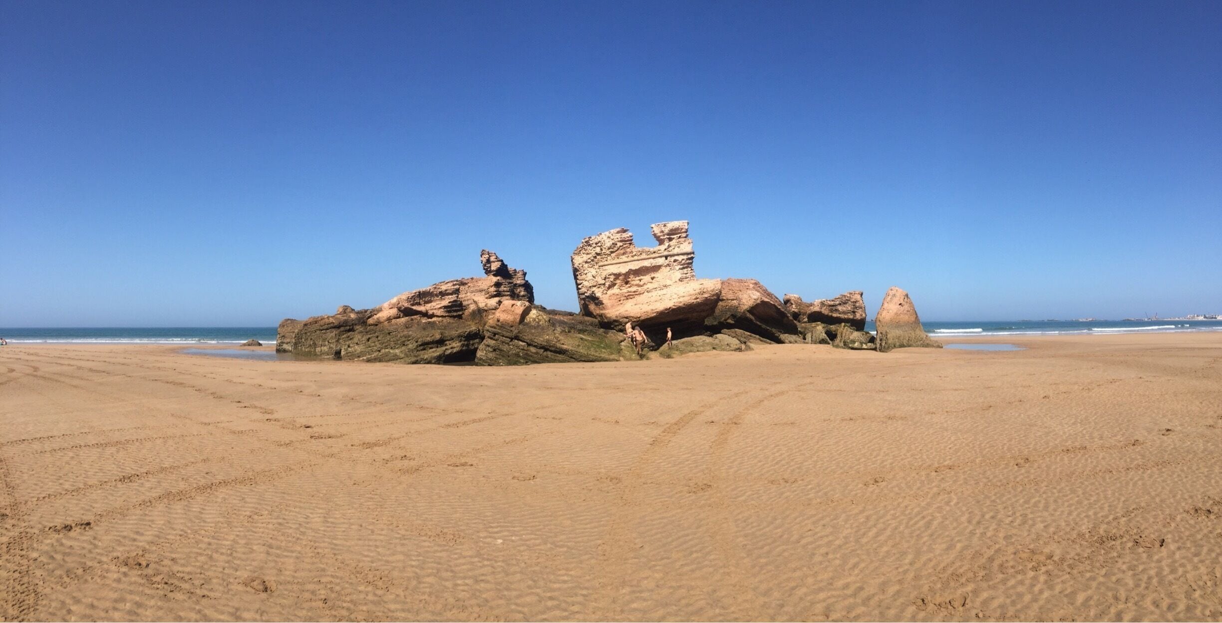 A sandy beach with large rock formations and the ocean in the background.