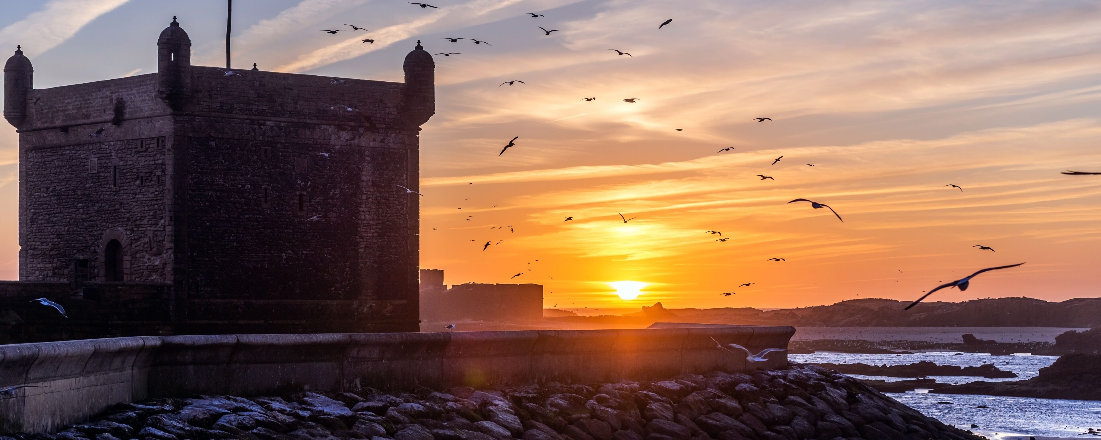 Panorama view of the silhouette from the old Fort Essaouira, Sqala du Port, at sunset, blue sky, background with flying Seagulls in Essaouira, Morocco