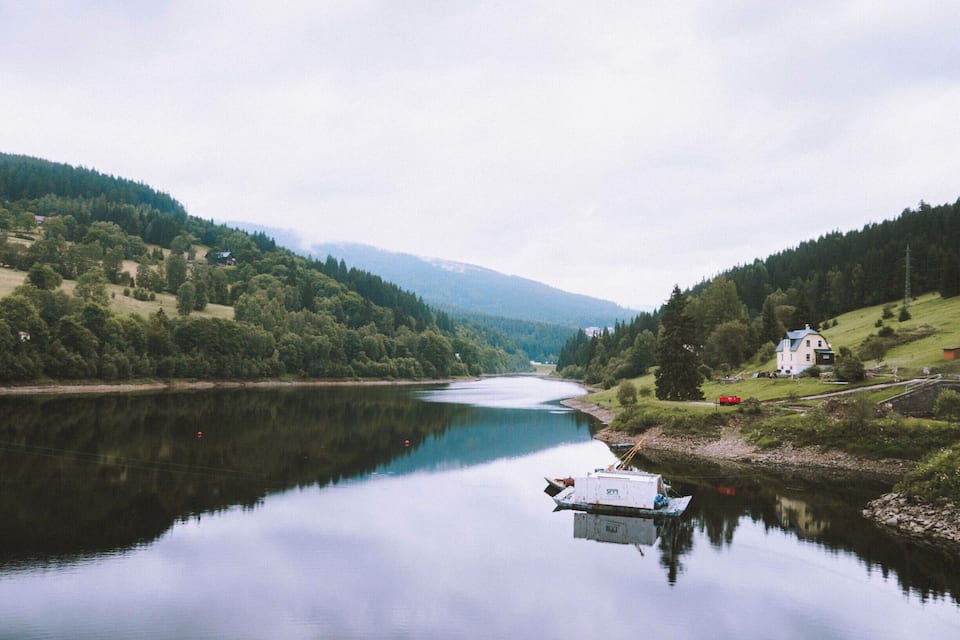 Un lac paisible avec une petite barque, entouré de collines verdoyantes et avec une maison sur la droite.