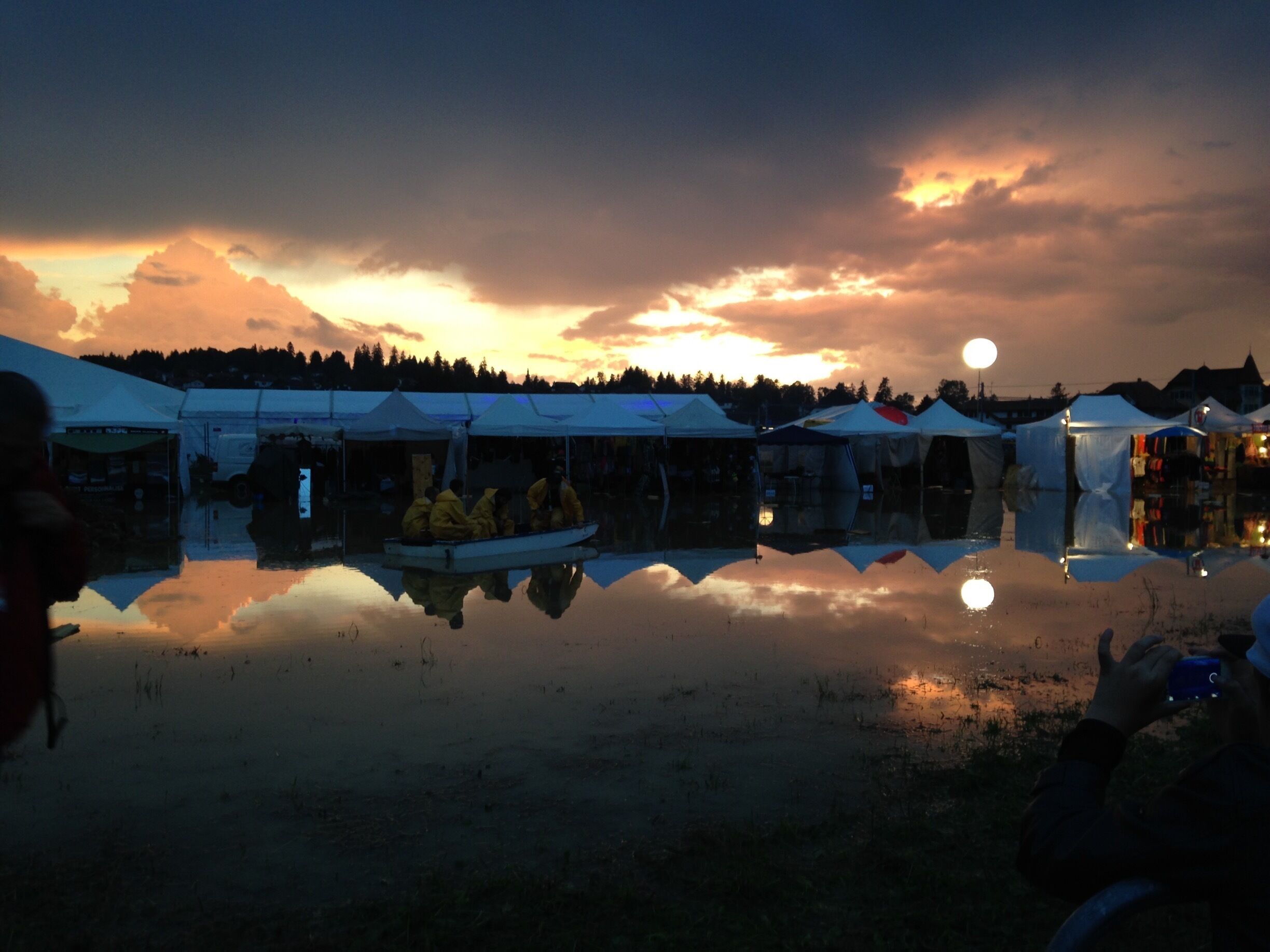 A sunset over a lake with tents and a boat reflecting the sky.