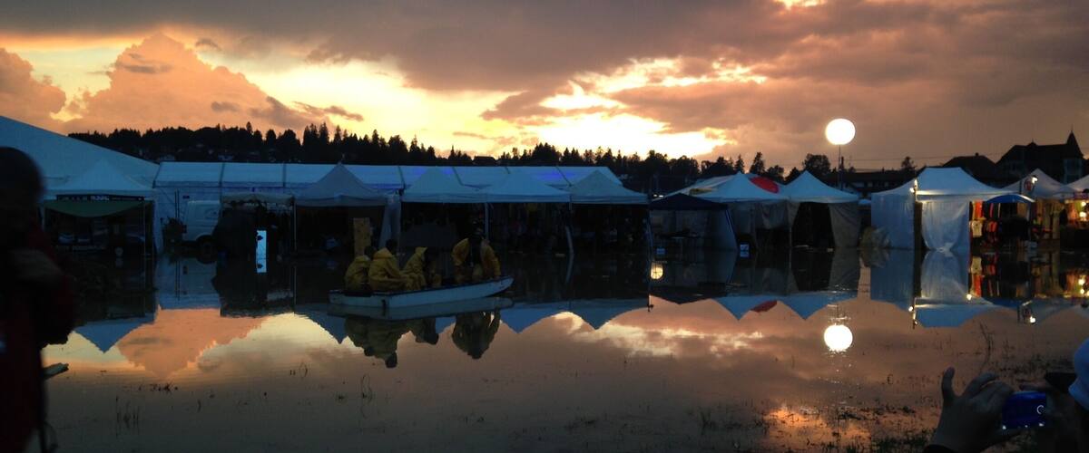 A sunset over a lake with tents and a boat reflecting the sky.