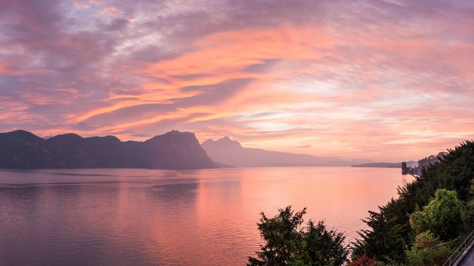 A calm lake with mountains in the background and a colorful sunset sky.