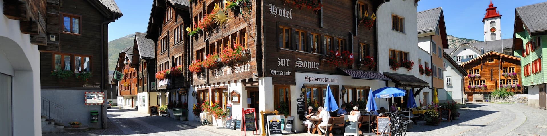 A traditional European town square with wooden buildings, flower boxes, and a clock tower.