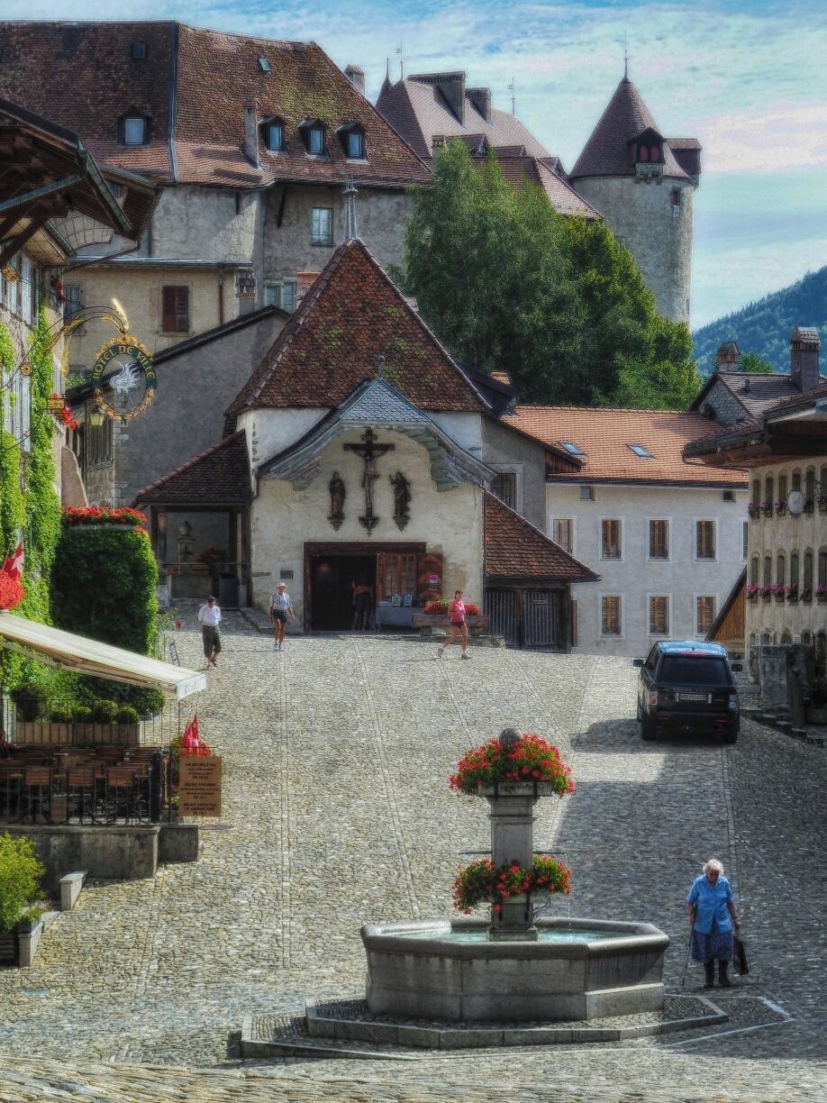 A cobblestone square with a fountain, historic buildings, and a castle in the background.
