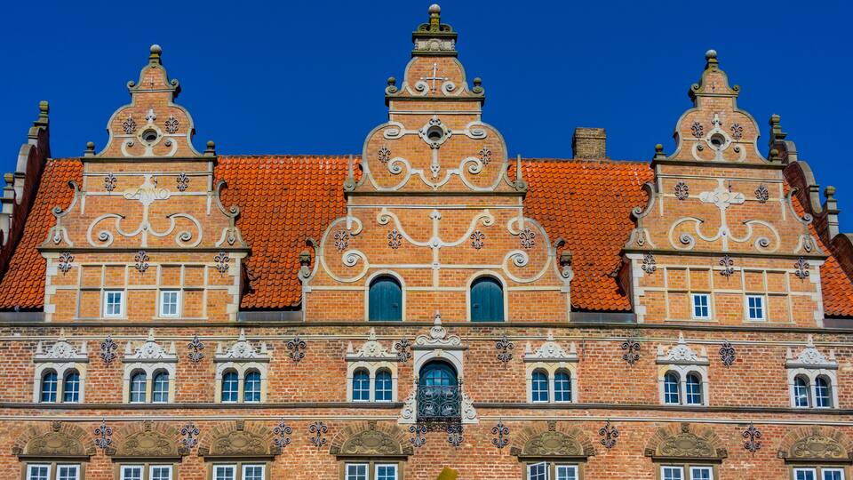 A historic building with ornate brickwork, red-tiled roof, and multiple windows.