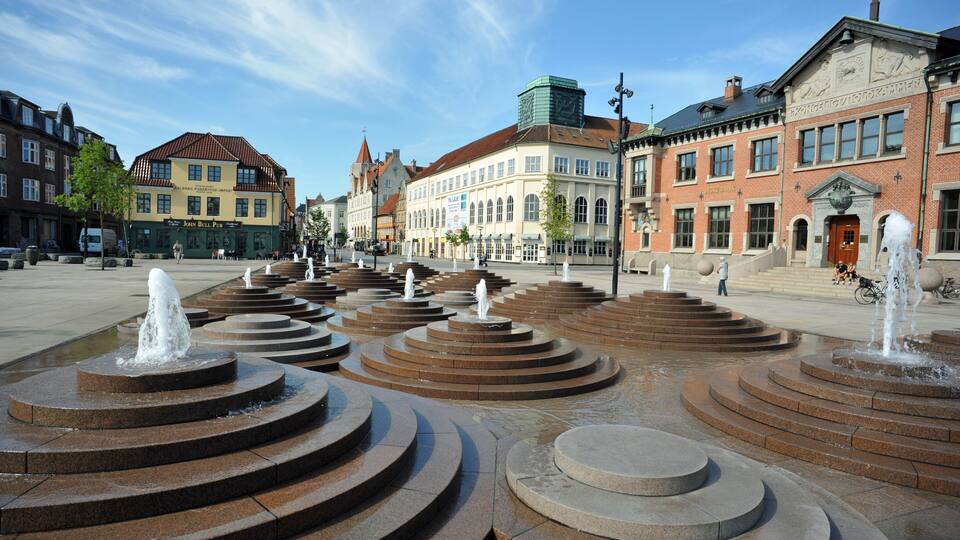 A public square with a central fountain, surrounded by historic buildings.