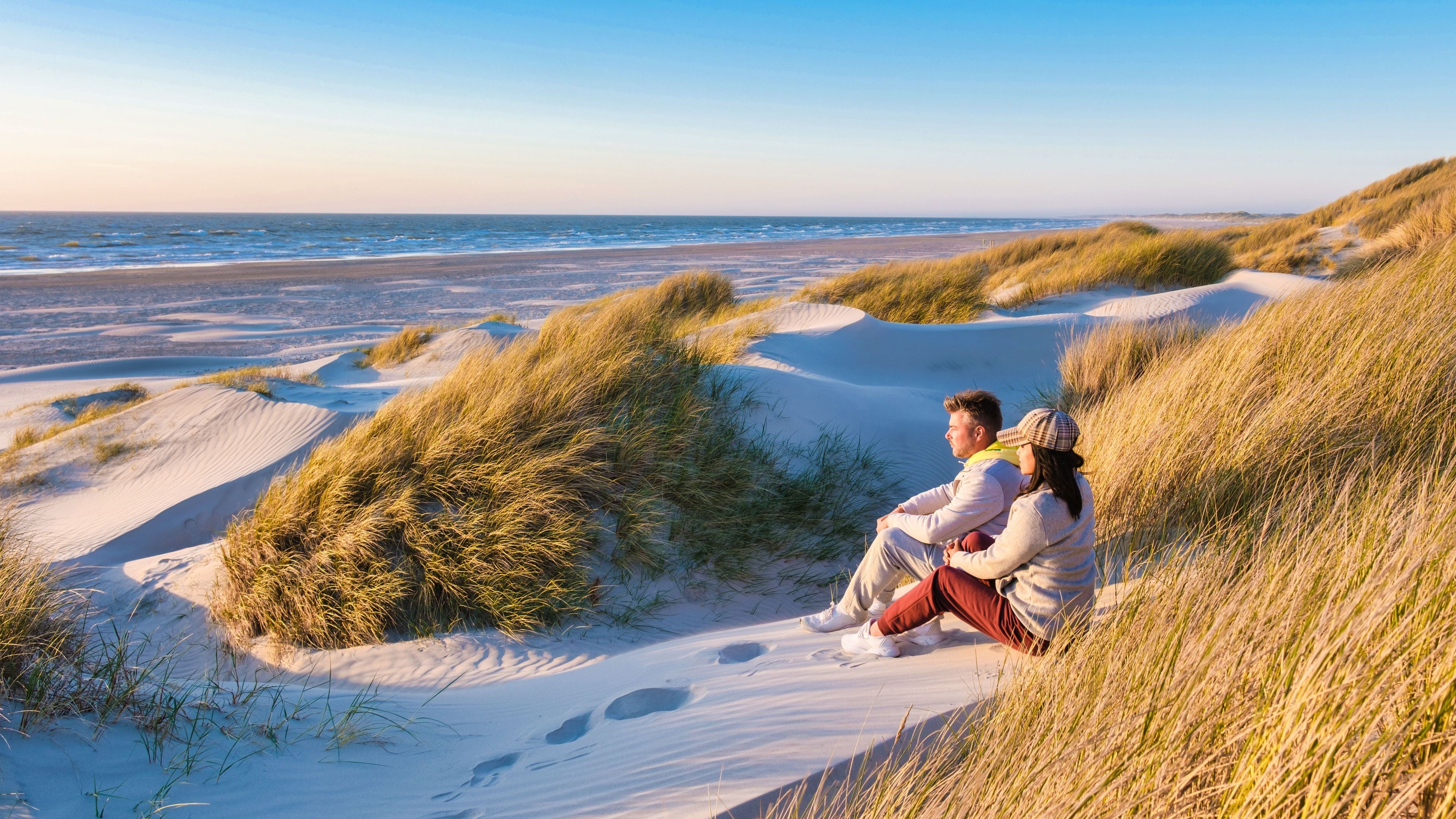 Una pareja sentada sobre dunas de arena con vistas a la playa.