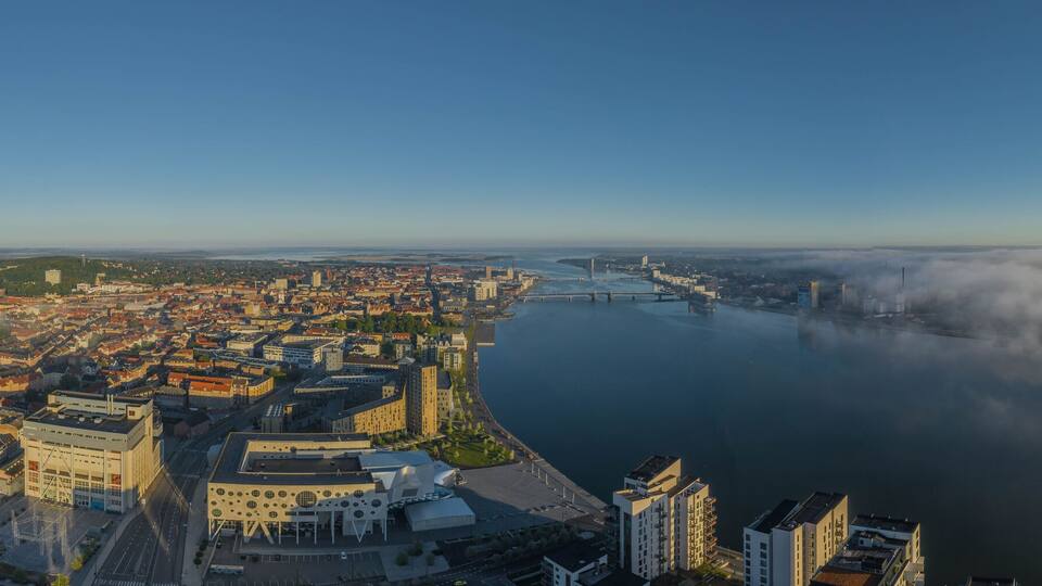 A panoramic view of a city with a river, bridges, and a fog-covered landscape.