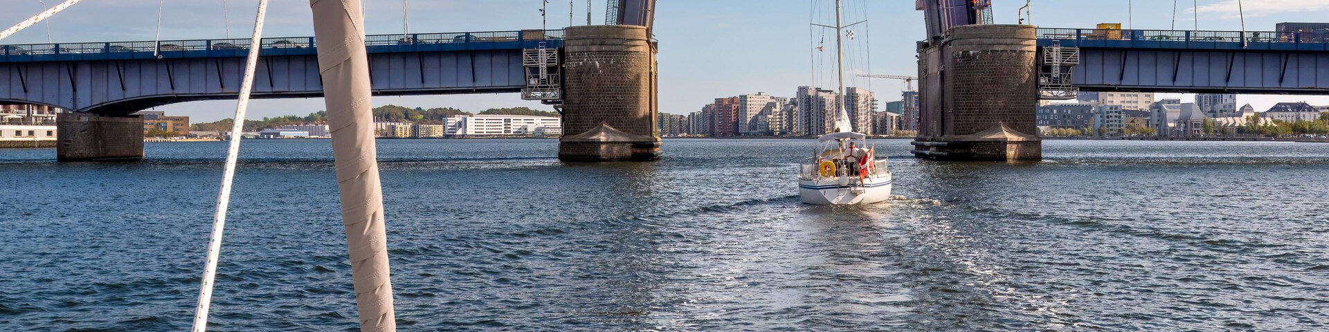 Un velero en un río, con un puente al fondo.