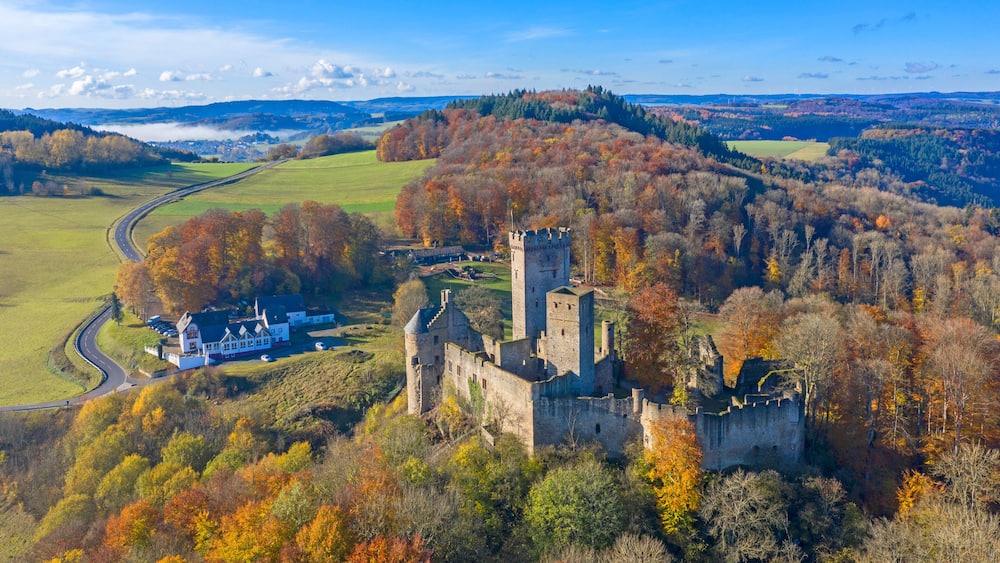 A historic castle surrounded by autumn-colored trees and a rural landscape.