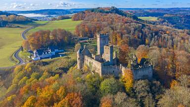A historic castle surrounded by autumn-colored trees and a rural landscape.