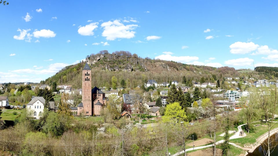 A town with a prominent church tower, a river, and surrounding greenery.