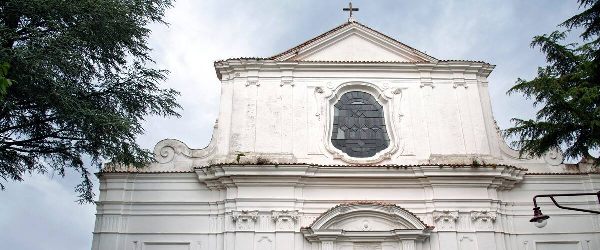 A white church with a cross on top, a large arched window, and a blue door.