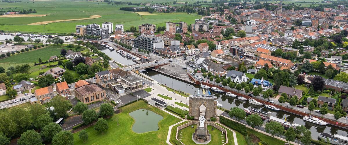 An aerial view of a town with a canal, a central monument, and surrounding greenery.
