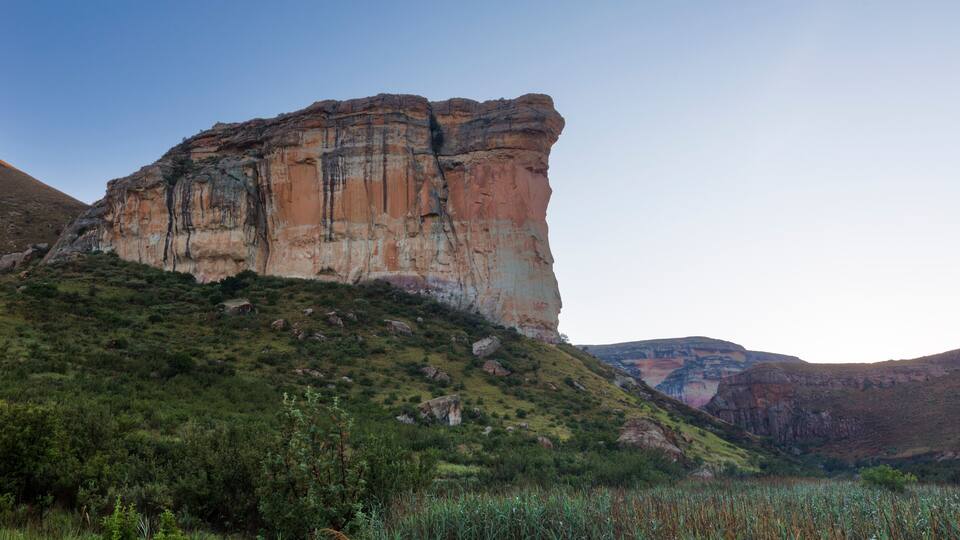 A large rock formation with a steep cliff and a grassy hill in the foreground.