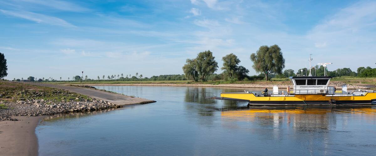 A yellow boat docked at a calm river with a bridge in the background and trees lining the shore.