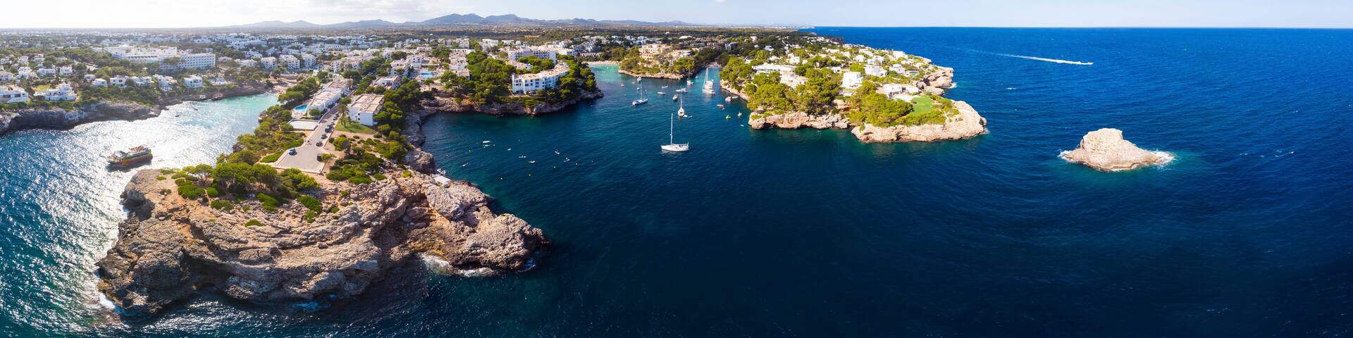 A coastal town with rocky outcrops, clear blue sea, and boats.