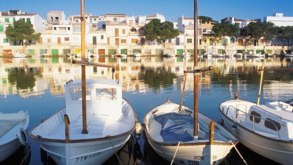 A marina with several boats docked, a clear sky, and buildings in the background.