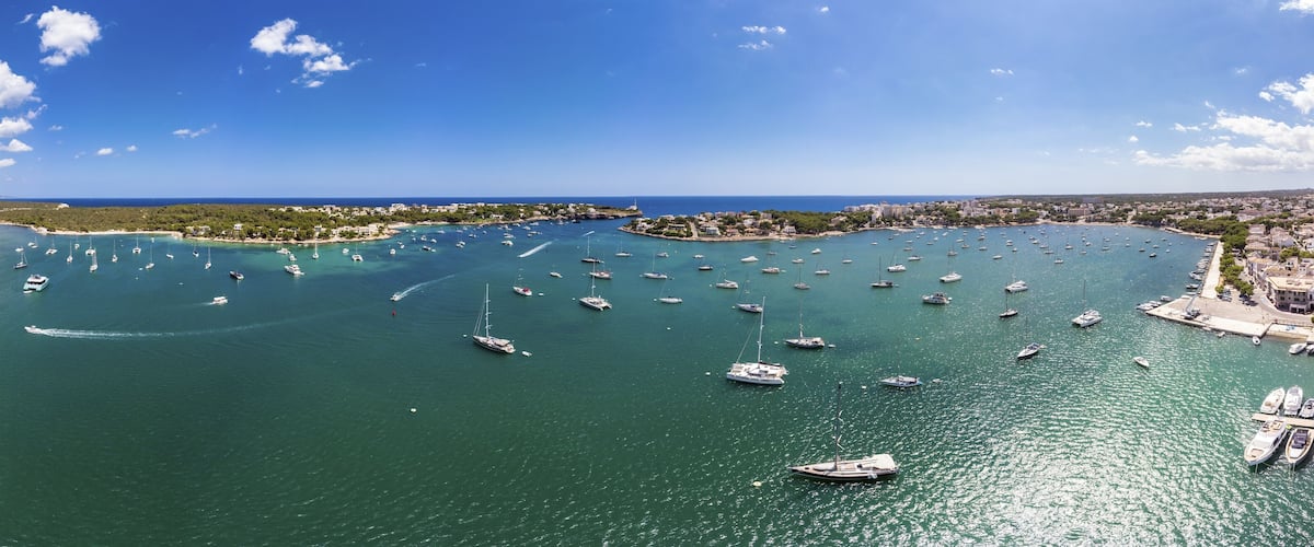 A coastal town with numerous sailboats docked along the shoreline and a clear blue sky.