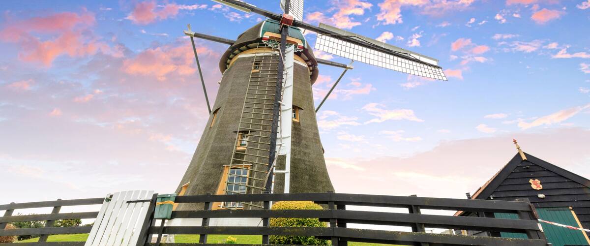 A windmill with a cross on top, surrounded by a wooden fence and a green building.