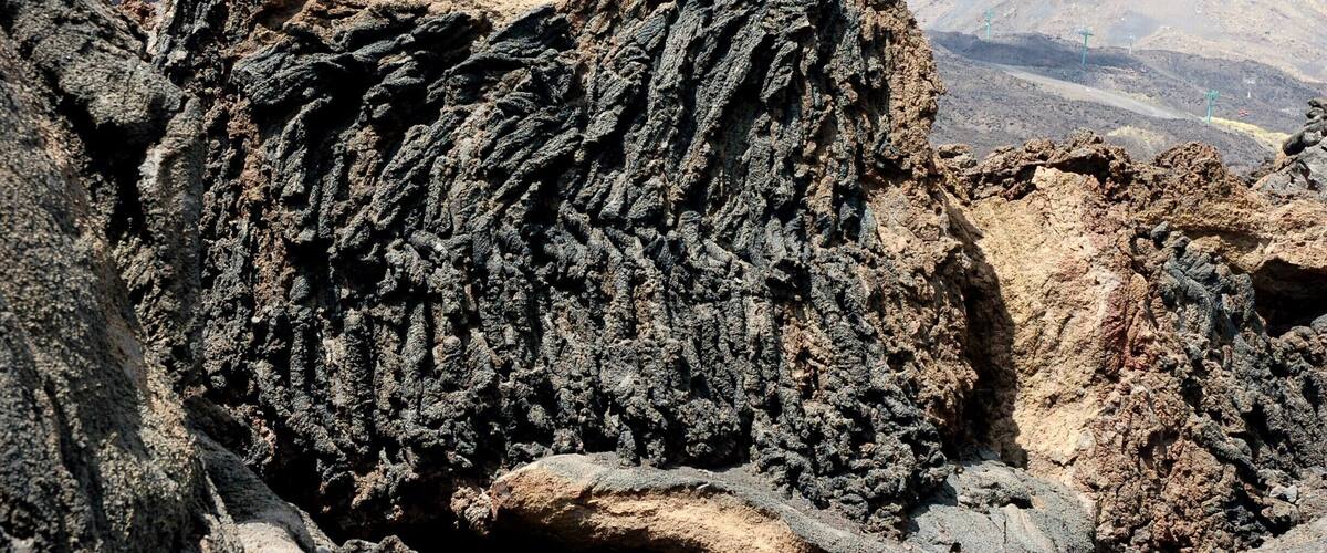 A rugged volcanic landscape with prominent rock formations and distant mountains.