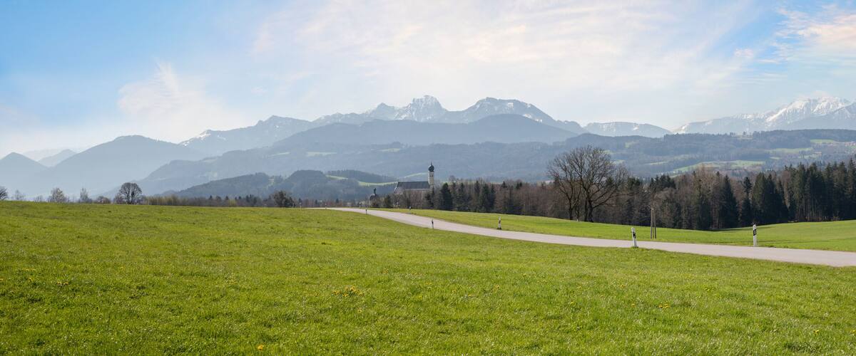 A grassy field with a paved path, a tower, and snow-capped mountains in the background.