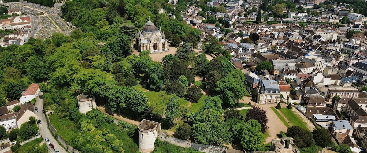 An aerial view of a historic park with a prominent church, castle ruins, and surrounding residential area.