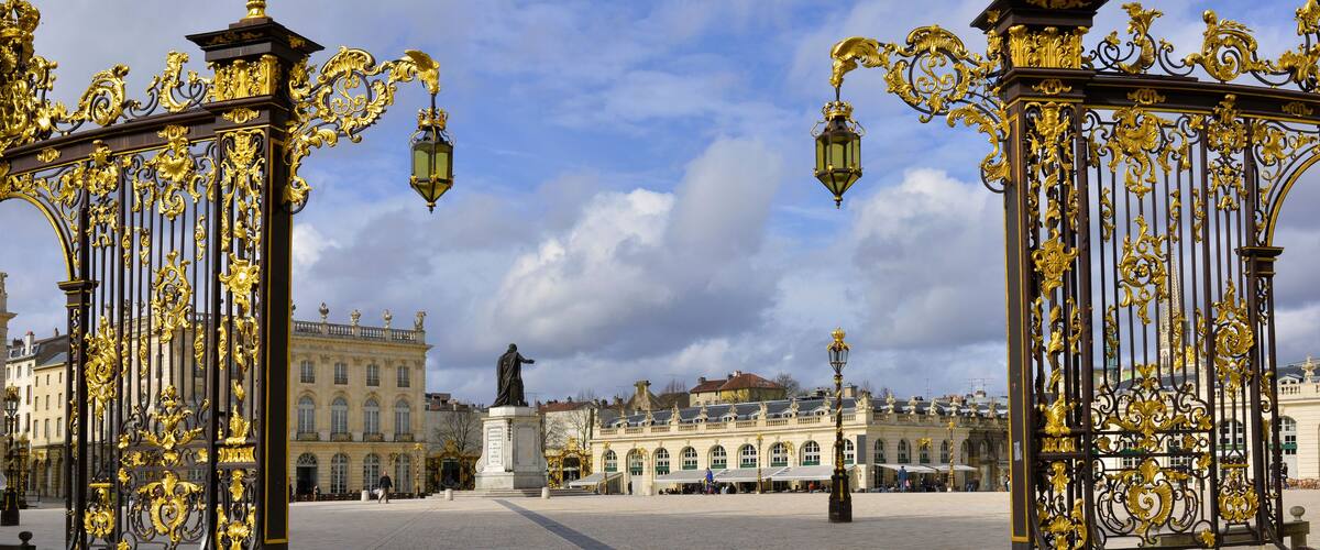 Ornate golden gates, a statue, and historic buildings in a square.
