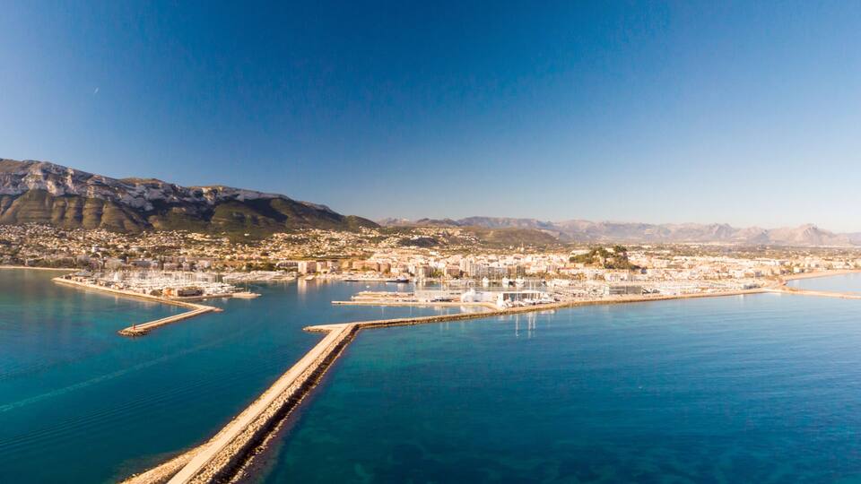 A coastal city with a prominent mountain, a marina, and a clear blue sea.