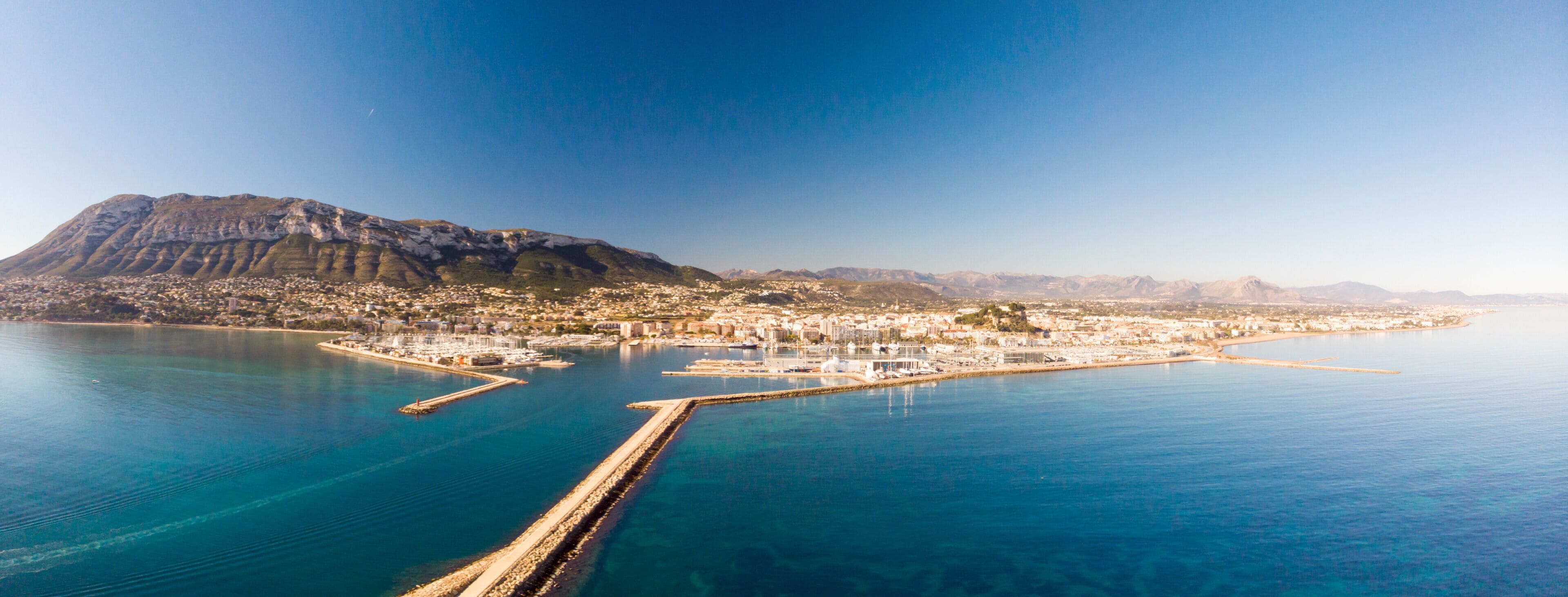 A coastal city with a prominent mountain, a marina, and a clear blue sea.
