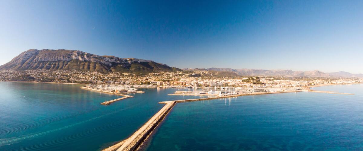A coastal city with a prominent mountain, a marina, and a clear blue sea.