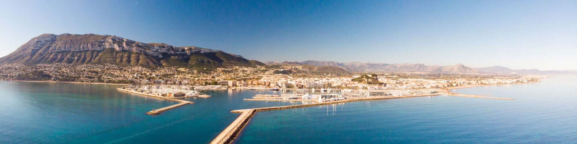 A coastal city with a prominent mountain, a marina, and a clear blue sea.
