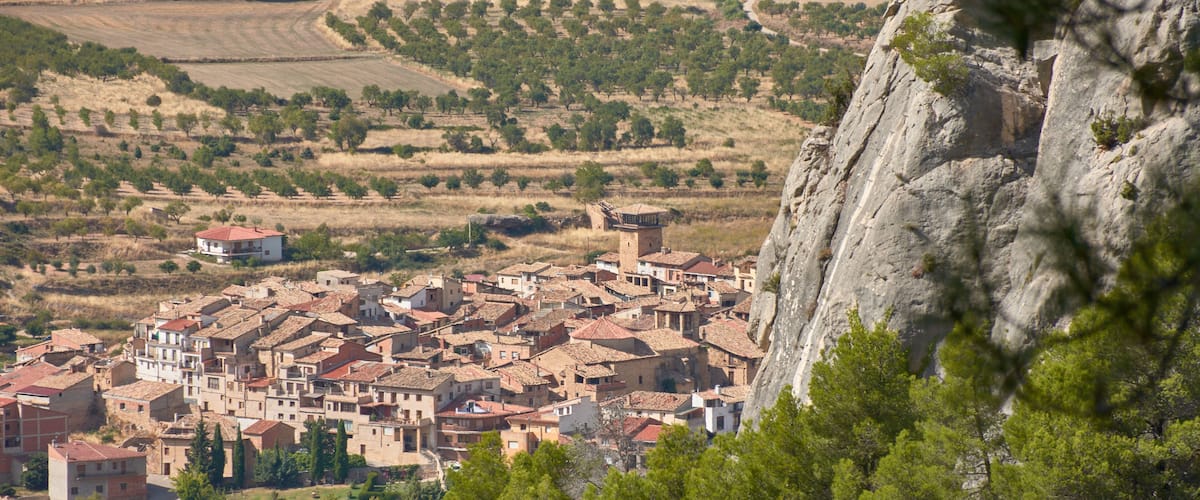 A town nestled in a valley with terraced fields and a prominent rock formation in the foreground.