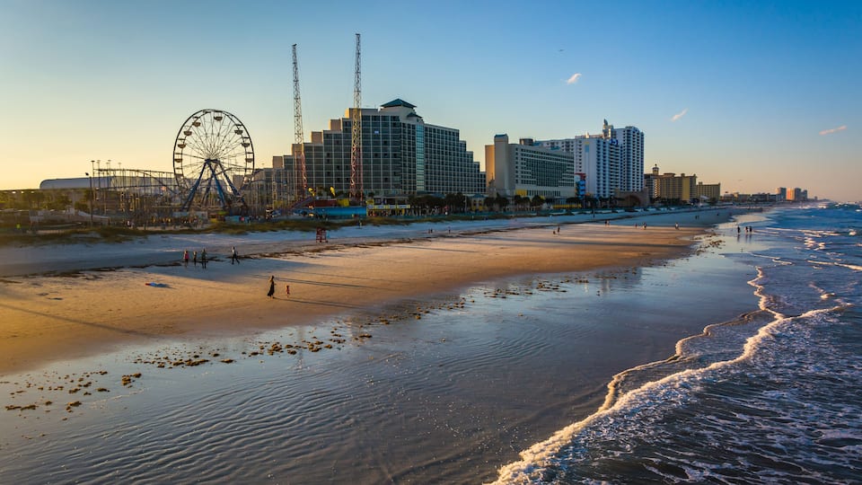A beach with a Ferris wheel and hotels in the background.