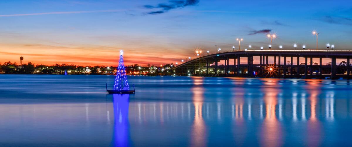 La silhouette d’une ville au crépuscule, un pont et un sapin de Noël illuminé de lumières bleues.