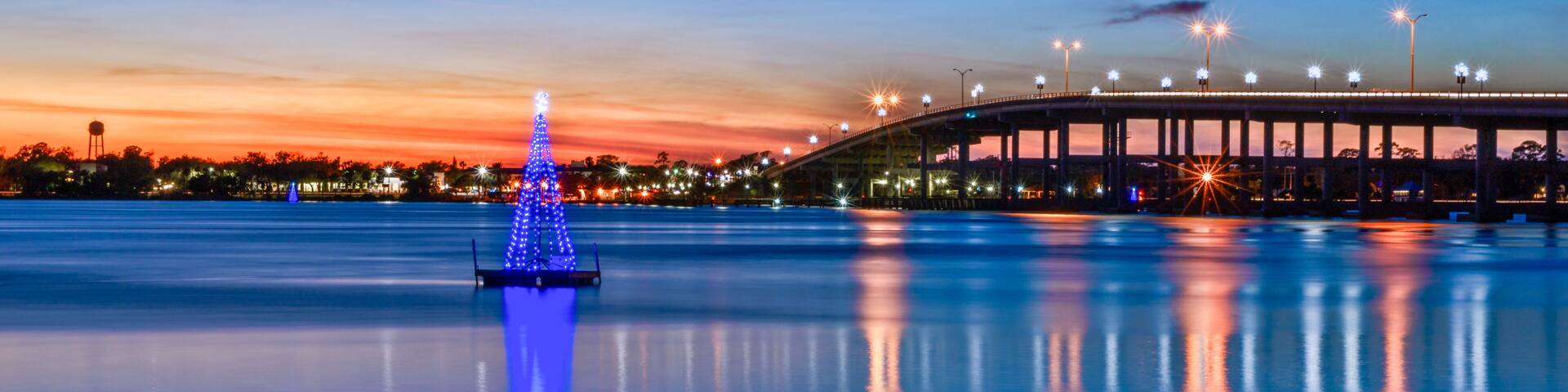 A city skyline at dusk, a bridge, and a Christmas tree illuminated by blue lights.