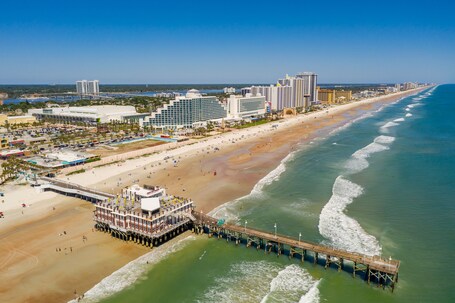 A coastal cityscape with a beach, pier, and high-rise buildings.
