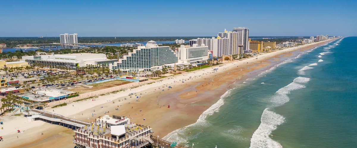 A coastal cityscape with a beach, pier, and high-rise buildings.