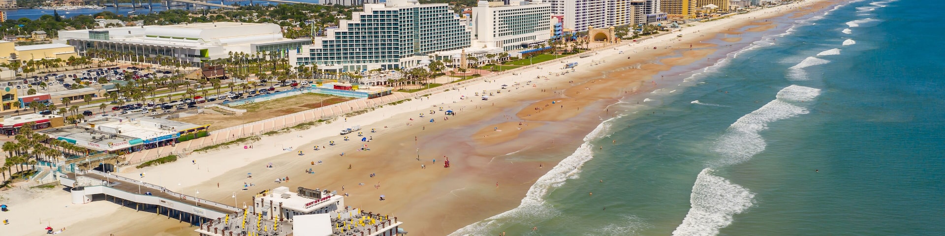 A coastal cityscape with a beach, pier, and high-rise buildings.