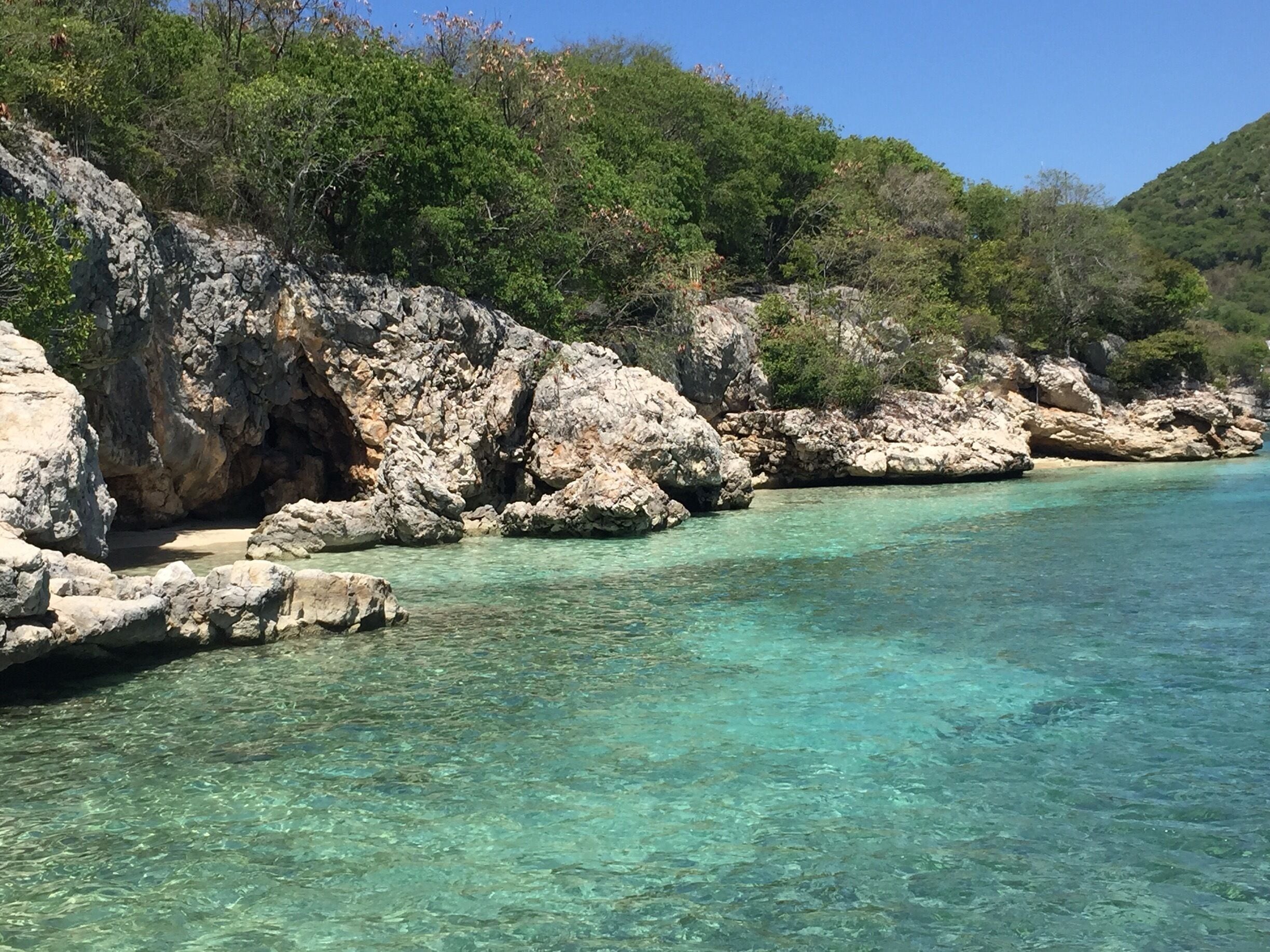 A clear turquoise sea with rocky cliffs and dense green foliage.